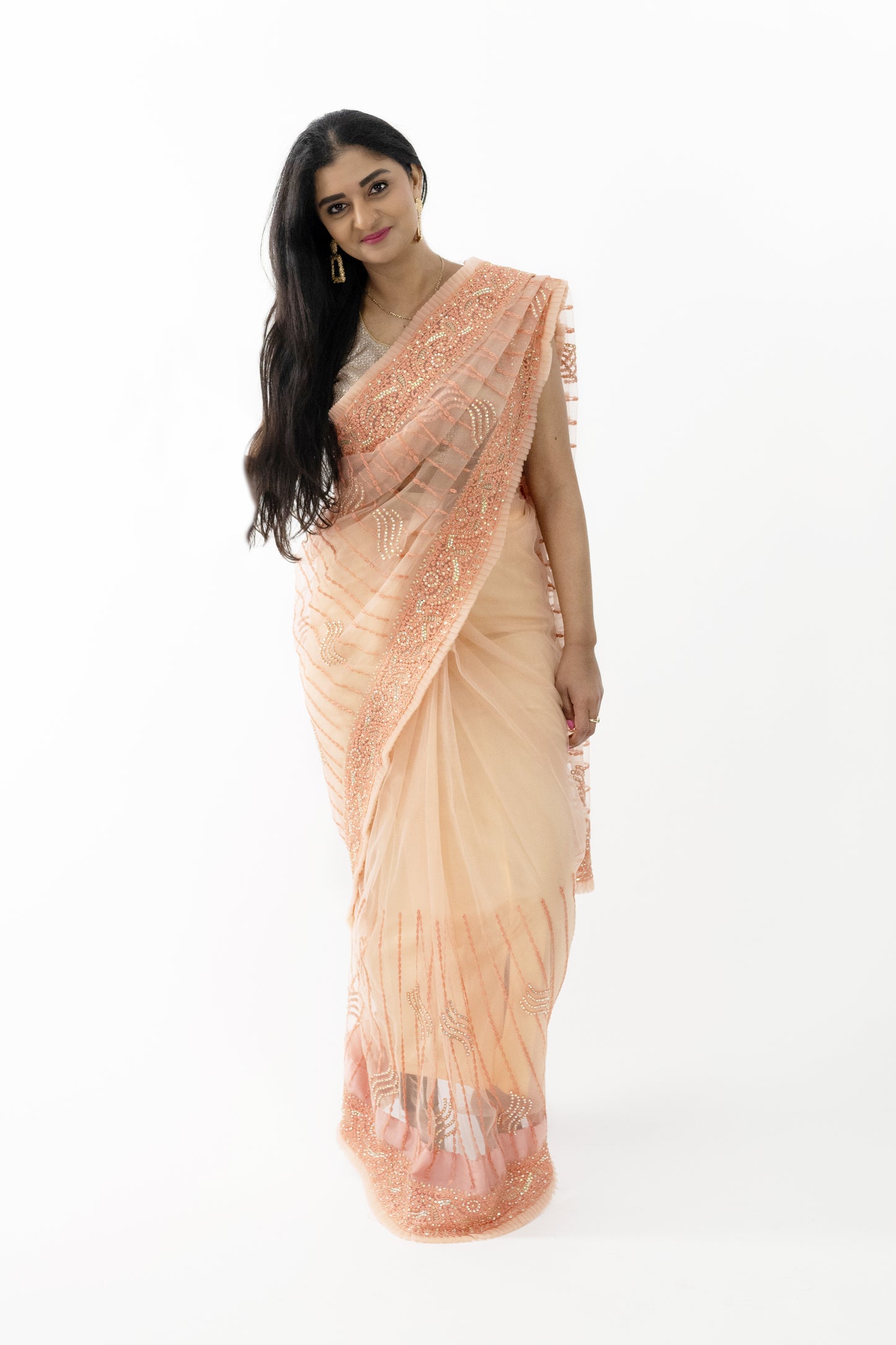 The image shows a person elegantly draped in a ready-to-wear peach net saree in Australia. The saree features intricate ship motifs that add a touch of nautical charm. The delicate net fabric is light and airy, providing a graceful and flattering silhouette. This saree is perfect for special occasions, exuding sophistication and elegance.