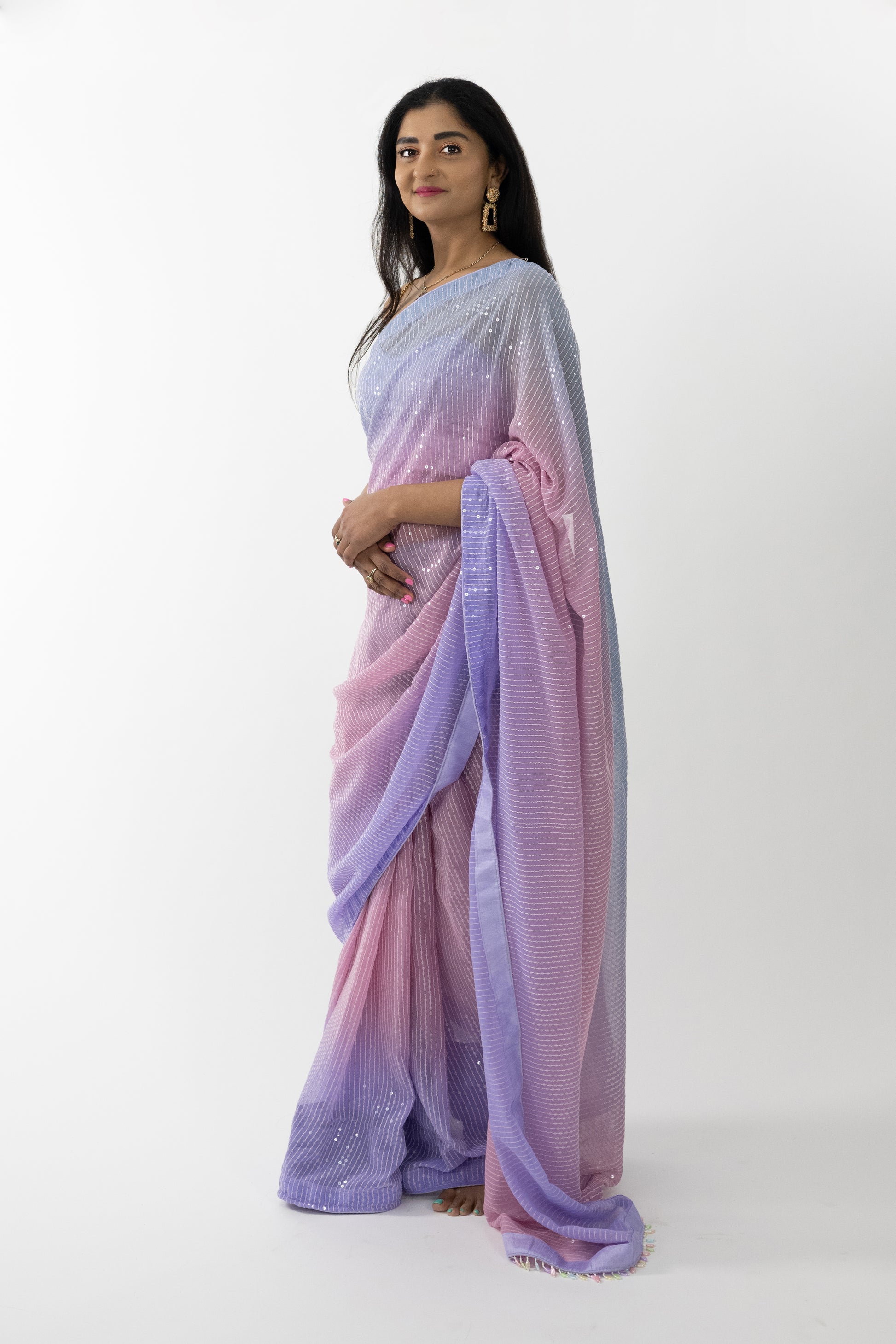  A full view of the “Sequin Dreams Georgette Saree” in a soft lavender hue, adorned with sequin details. The saree’s luxurious georgette fabric is light, airy, and beautifully draping, providing a comfortable and flattering fit. The serene lavender color evokes calm and elegance, perfect for creating a refined look. This ready-to-wear saree is ideal for special occasions in Australia