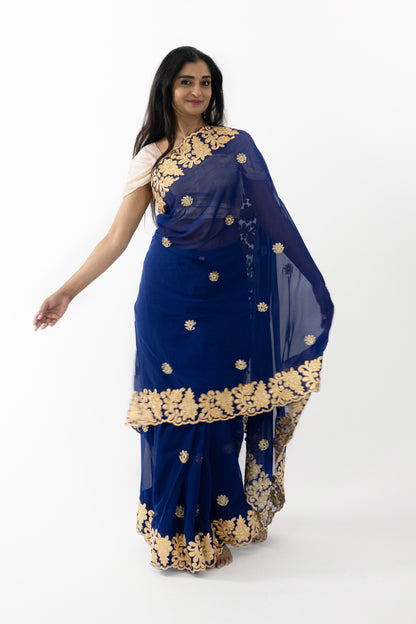 The image captures a person showcasing the beautiful drape of the navy blue georgette saree. The saree’s intricate gold detailing and soft, lightweight fabric create a graceful and sophisticated appearance. Ideal for weddings, receptions, and festive gatherings, this saree exudes timeless beauty and elegance.