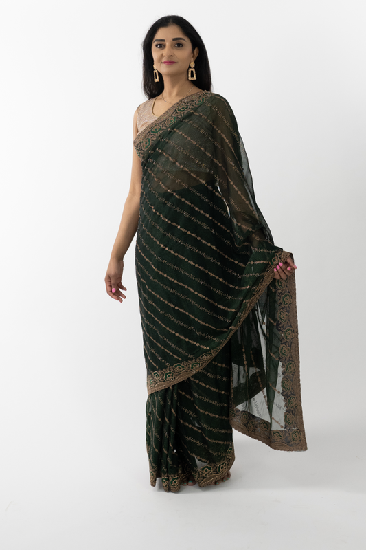 The image shows a person elegantly draped in a ready-to-wear dark green Simar silk saree in Australia. The saree features intricate gold embroidery that showcases meticulous craftsmanship. The rich texture and elegant drape of the Simar silk add a touch of opulence. This saree is perfect for special occasions, exuding sophistication and grace.