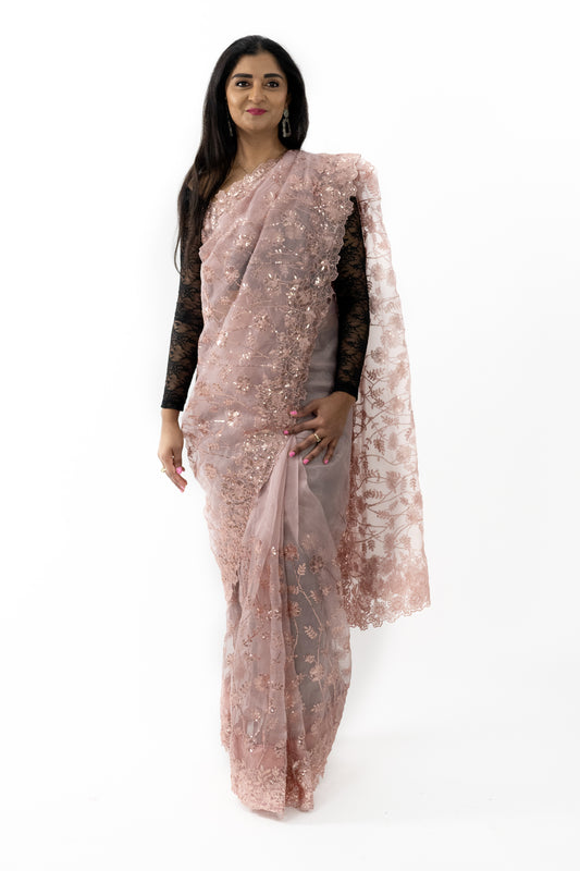 The image shows a person elegantly draped in a ready-to-wear peach organza saree in Australia. The saree features intricate detailing that showcases exquisite craftsmanship. The light and airy organza fabric provides a sheer and elegant look. This saree is perfect for special occasions, exuding grace and refinement
