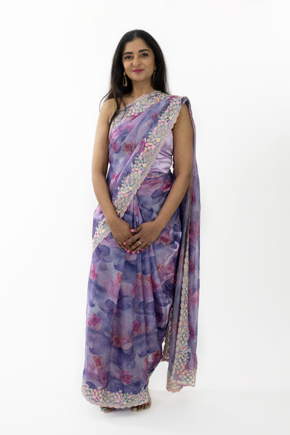 The image shows a person elegantly draped in a ready-to-wear purple silk saree in Australia. The saree features intricate floral patterns that showcase meticulous craftsmanship. The luxurious silk fabric is soft and smooth, providing a comfortable and elegant fit. This saree is perfect for grand occasions, exuding sophistication and grace.