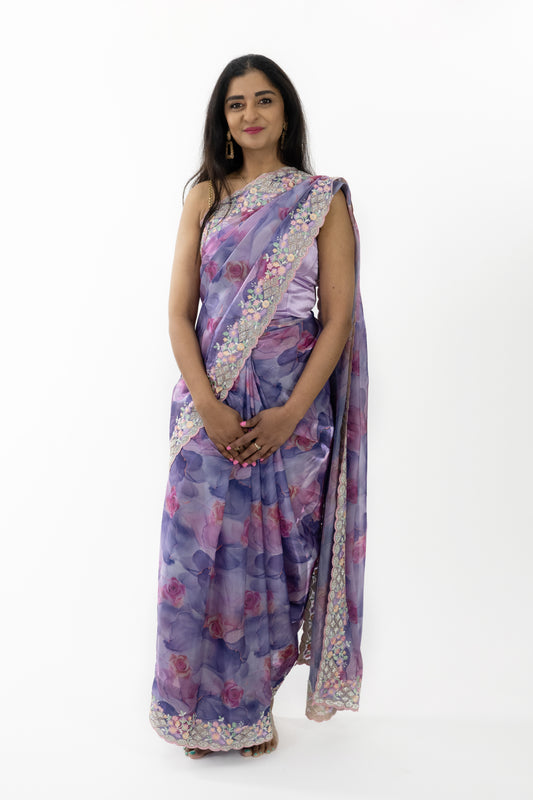 The image shows a person elegantly draped in a ready-to-wear purple silk saree in Australia. The saree features intricate floral patterns that showcase meticulous craftsmanship. The luxurious silk fabric is soft and smooth, providing a comfortable and elegant fit. This saree is perfect for grand occasions, exuding sophistication and grace.