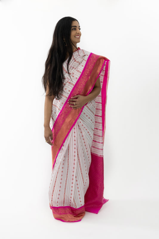  The image shows a person elegantly draped in a ready-to-wear white Banarasi silk saree in Australia. The saree features intricate pink detailing and motifs, showcasing fine craftsmanship. The rich texture and lustrous finish of the Banarasi silk add a touch of royal elegance. This saree i
